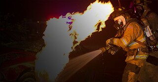 A firefighter spraying water on a burning car
