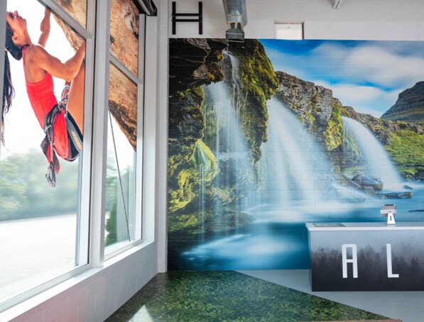 Interior de una tienda de ropa deportiva, con una pared decorada con la imagen de una cascada al fondo.