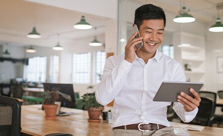 Imagen de un empresario sonriente hablando por teléfono y mirando una tableta.
