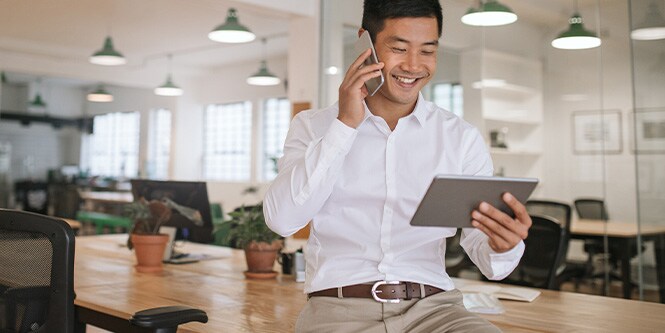 Imagen de un empresario sonriente hablando por teléfono y mirando una tableta.

