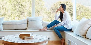 Clear, crisp sunlight fills a sunroom as a woman rests comfortably on a window seat.