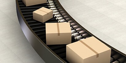 Imagen de cajas cerradas moviéndose a lo largo de una cinta transportadora curva.
