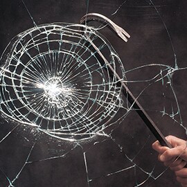 A close-up view of a crowbar hitting a window, causing it to crack but not shatter due to the security film