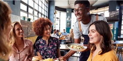 Un camarero lleva la comida a cuatro clientes sonrientes.
