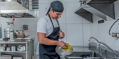 Un trabajador de cocina comercial frota una sartén en un fregadero.
