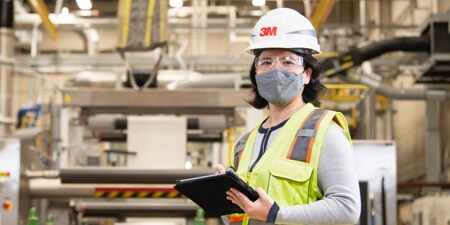 3M plant employee wearing a hard hat, wearing a bright yellow safety vest.
