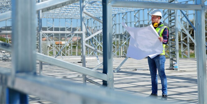 Dos trabajadores con chalecos de alta visibilidad y cascos están en una instalación industrial luminosa rodeados de grandes tuberías, válvulas y equipos de procesamiento.