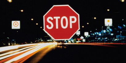 A stop sign reflects brightly against a backdrop of nighttime road traffic. 
