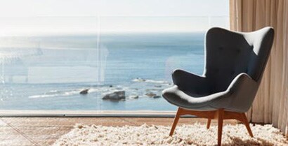 A special chair is placed in front of floor to ceiling windows that look out at the ocean.
