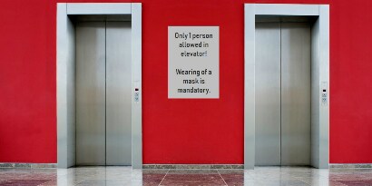 Imagen de las puertas de dos ascensores con puertas cerradas. Paredes rojas y piso gris brillante.
