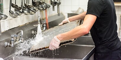 Un lavaplatos de restaurante limpiando una bandeja en un fregadero comercial.
