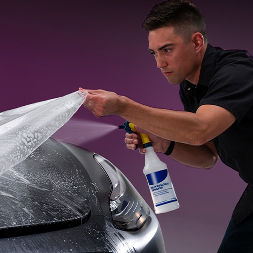 Man spraying water during paint protection installation on hood of car
