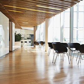 An office space with abundant natural light shining through large windows and featuring wooden flooring.