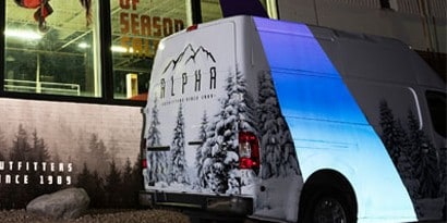Imagen de una camineta blanca estacionada. Ploteada con pinos nevados y una franja luminosa
