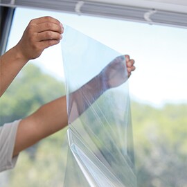 An individual holding a single sheet of window film preparing to apply it onto a window surface.