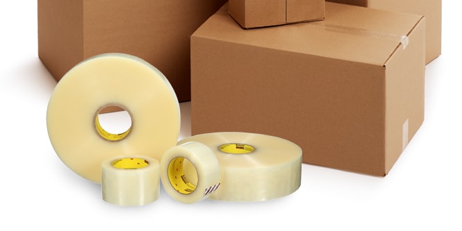 Cuatro rollos de cintas transparentes de diferentes tamaños frente a cajas de cartón.
