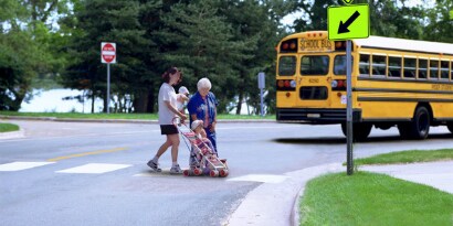 A family crosses the street near a pedestrian crossing sign. The road sign is highly visible to protect pedestrians.
