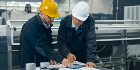 Dos personas usando cascos mirando una tableta sobre una mesa.
