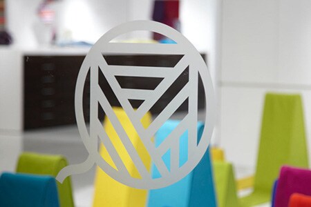Ventana de vidrio transparente con logotipo en líneas de estilo vidrio grabado con formas coloridas en el fondo.
