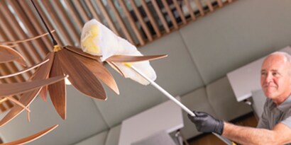 Employee dusting the top of a light fixture.
