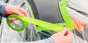 Manos aplicando cinta de enmascarar verde 3M en un vehículo preparado para pintura.
