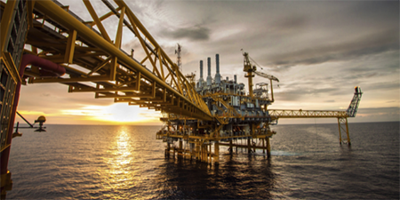 Plataforma petrolera en el océano al atardecer.
