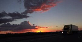 Imagen de un camión sobre carretera junto al atardecer