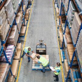 Vista aérea de trabajadores transfiriendo cajas de un pallet a una estantería.