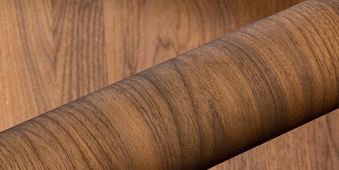 Rollo de acabado de vetas de madera arquitectónica DINOC sobre un fondo de vetas de madera.
