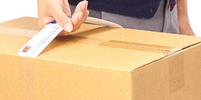 Un primer plano de la mano de una persona sosteniendo una caja de cartón con una asa.
