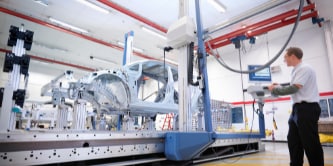 Persona trabajando en la pantalla de una máquina en el interior de una fábrica con máquinas.
