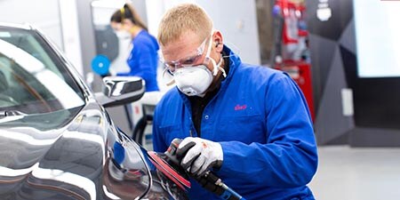 Un trabajador utilizando una lijadora rotorbital en la carrocería de un automóvil en un taller
