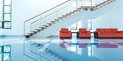 Instalación con escaleras marrones, tres sillones color ladrillo y piso brillante azul.

