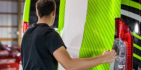 Instalador colocando película adhesiva verde lima y blanca sobre una camioneta.
