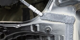 A grey seam sealer bead being applied to the body of a car.
