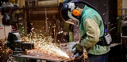 Trabajador con equipo de protección usando una amoladora, generando chispas.

