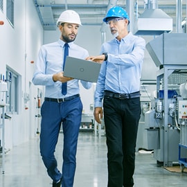 Dos empleados de una fábrica caminando y hablando de trabajo con una laptop en la mano con Logotipo de 3M.