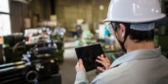 Persona con casco blanco sosteniendo una tableta y tocando la pantalla.

