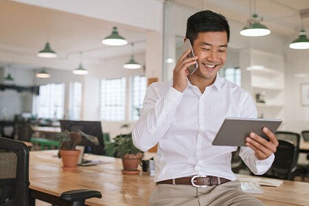 Imagen de un empresario sonriente hablando por teléfono y mirando una tableta.
