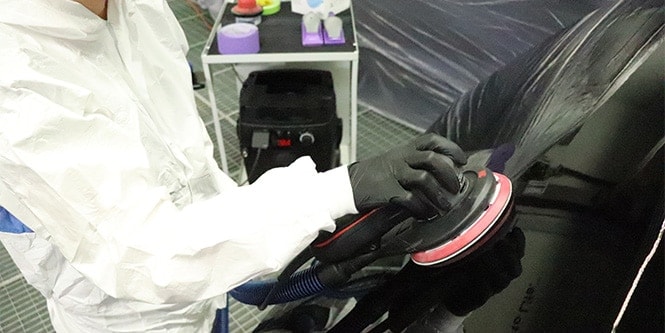 Trabajador en un taller utilizando una lijadora del Sistema de Lijado Limpio de 3M en la superficie de un vehículo.
