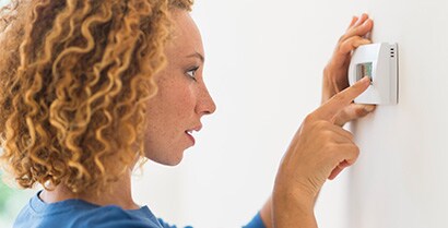 A young woman adjusts the temperature on her thermostat.
