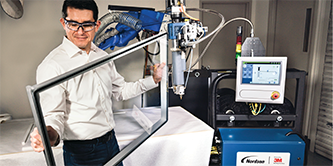 Imagen de un hombre sosteniendo un marco al que se le ha aplicado Cinta Extrudible 3M™ VHB por el robot en el fondo.
