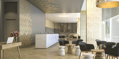 Recepción con paredes grises, vinilos dorados, mesa marmolada, sillones negros y banquetas blancas.
