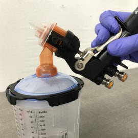 Mano con guantes sosteniendo una pistola de pulverización conectada a un vaso de pintura PPS.