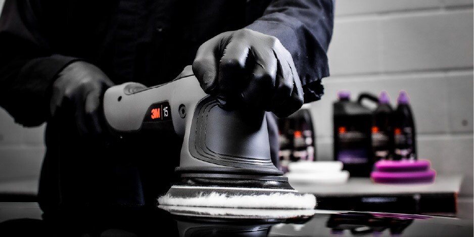 Persona utilizando una pulidora eléctrica con guantes negros sobre la superficie de un vehículo.
