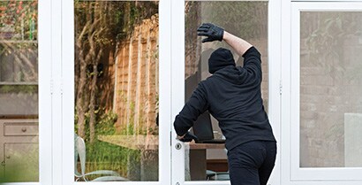 A person dressed in all black tries to look into a home he might want to rob through a window with reflective, security-enhancing window films.
