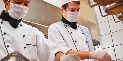 Dos cocineros con máscaras trabajando.
