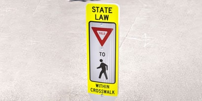 Sign with letters and symbols reading “State law: Yield to pedestrians in crosswalk.”
