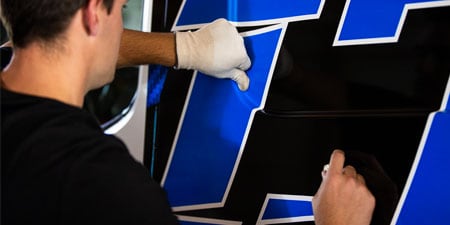 Instalador colocando película adhesiva azul y negro sobre una camioneta.
